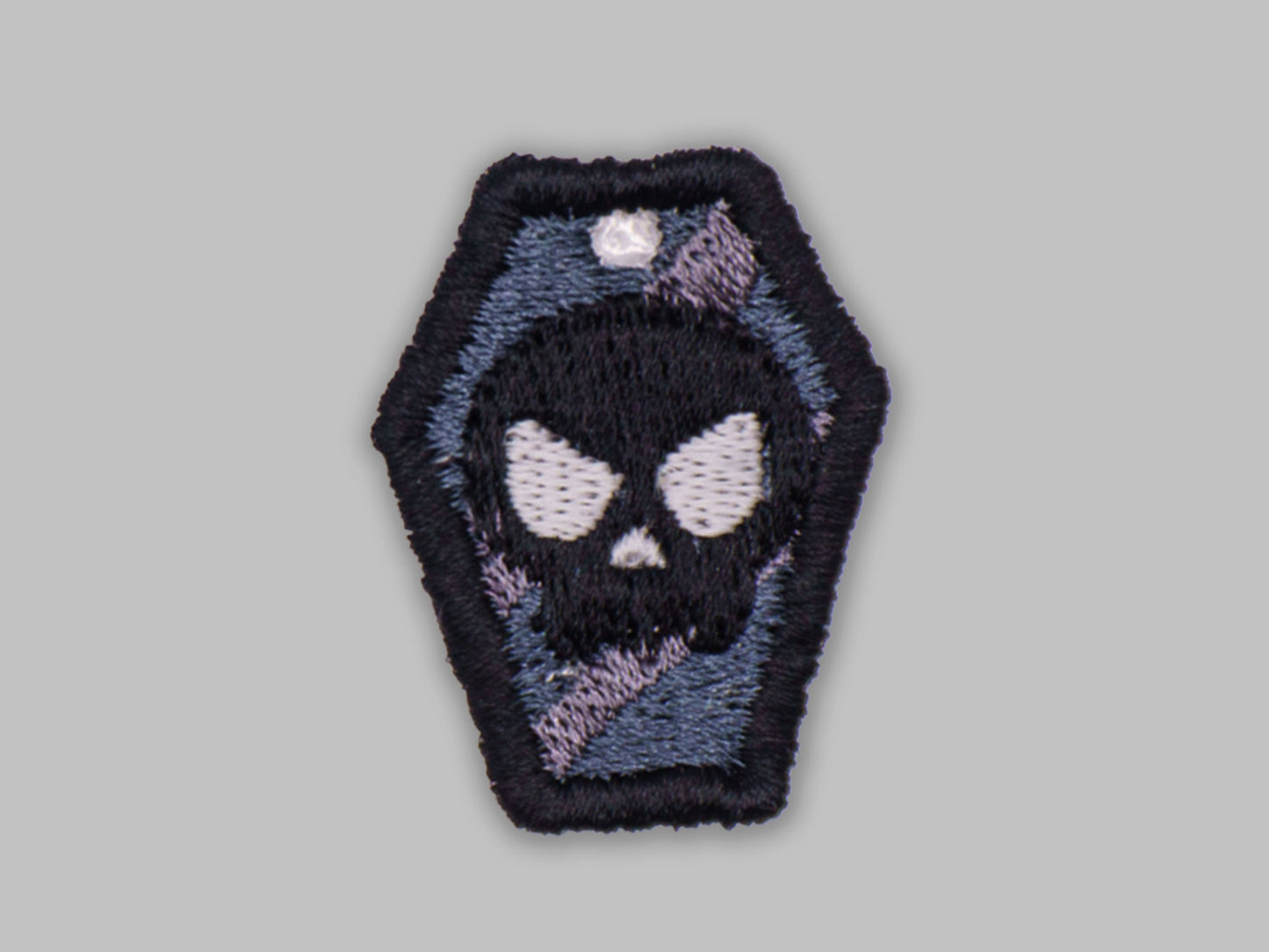 Embroidered patch of a skull in a coffin on a gray background