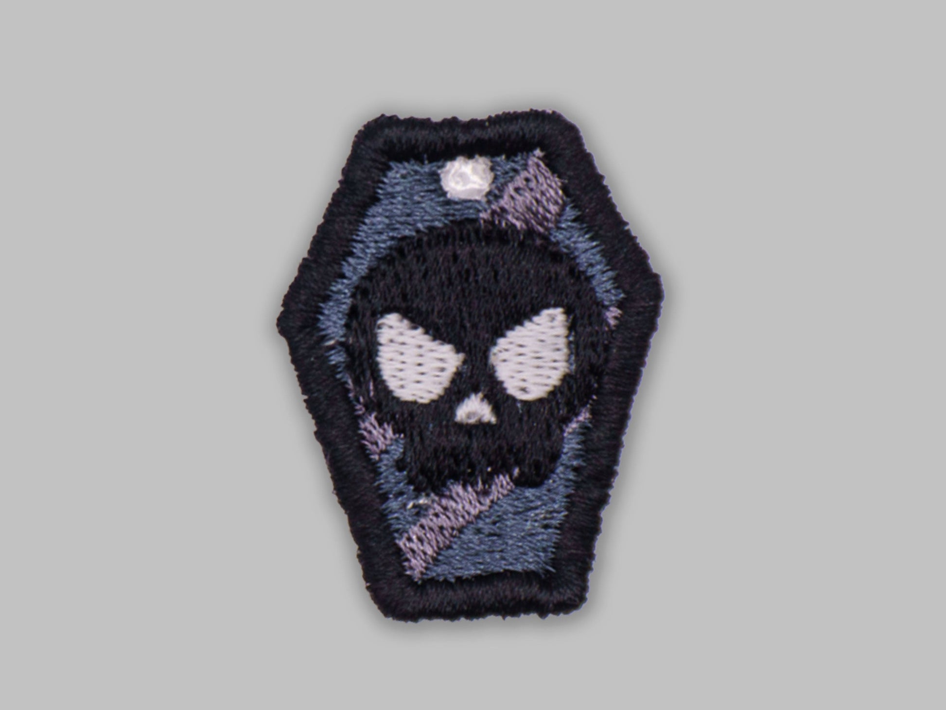 Embroidered patch of a skull in a coffin on a gray background
