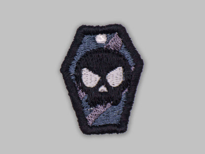 Embroidered patch of a skull in a coffin on a gray background